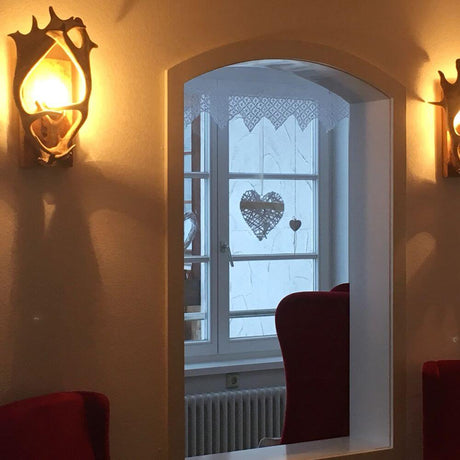 Damhirsch Chalet Geweih Wandlampe in einem stilvollen Innenraum mit Fenster und herzförmigem Dekor.
