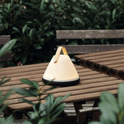 LED Akkuleuchte Strap ToGo IP54 Dimmbar auf einem Holztisch in einem Gartenumfeld.