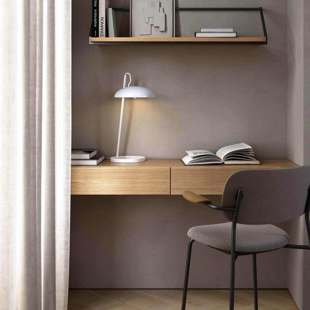 Versale Tischleuchte auf einem minimalistischen Schreibtisch mit Holzoberfläche und Bücherregal im Hintergrund.