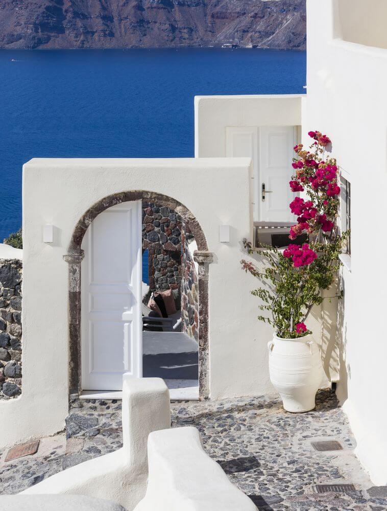 Ein architektonischer Blick auf ein weißes Gebäude mit einem Bogen und blühenden Pflanzen in Santorin.