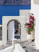 Ein architektonischer Blick auf ein weißes Gebäude mit einem Bogen und blühenden Pflanzen in Santorin.