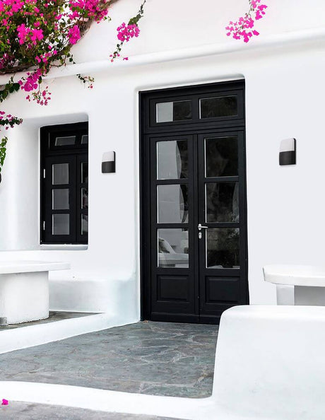 Modern Droplet LED outdoor wall light 3000K next to a black front door with blooming plants.