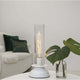 E27 Filament LED Soft Glow 2200K in einer modernen Tischlampe mit Pflanzen im Hintergrund.