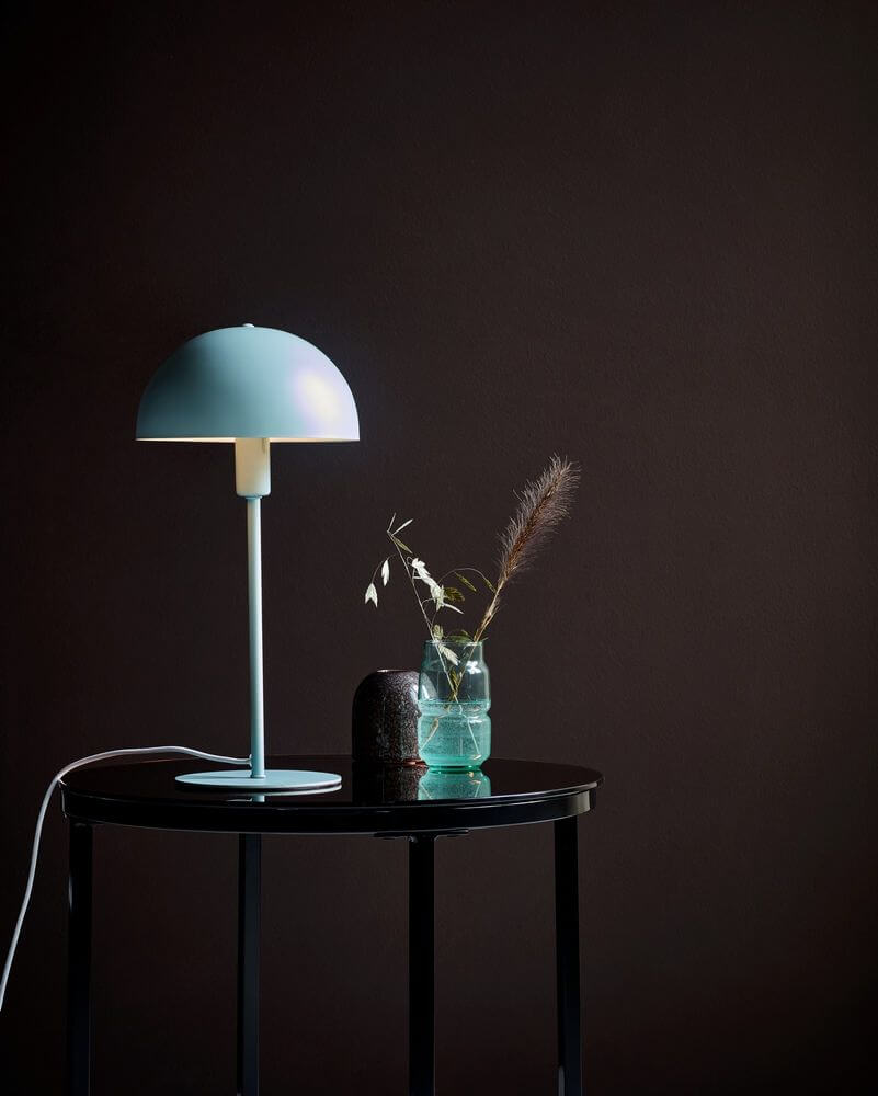 Ellen 20 Tischlampe auf einem schwarzen Tisch mit Vase und dekorativen Elementen im Hintergrund.