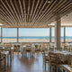Moderne Restaurant mit Meerblick, hellen Holztischen und eleganter Inneneinrichtung nahe dem Strand.