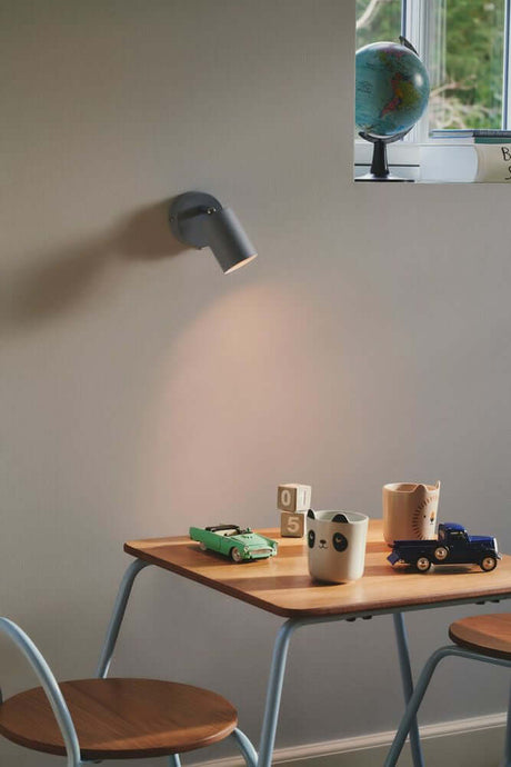 L'applique murale Explore de Nordlux diffuse une lumière douce au-dessus d'une table dans la chambre d'enfant.