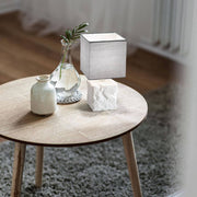 Adda Tischleuchte E14 Weiß auf einem Holz Tisch neben einer Vase und einem runden Teppich.