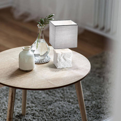 Adda Tischleuchte E14 Weiß auf einem Holz Tisch neben einer Vase und einem runden Teppich.