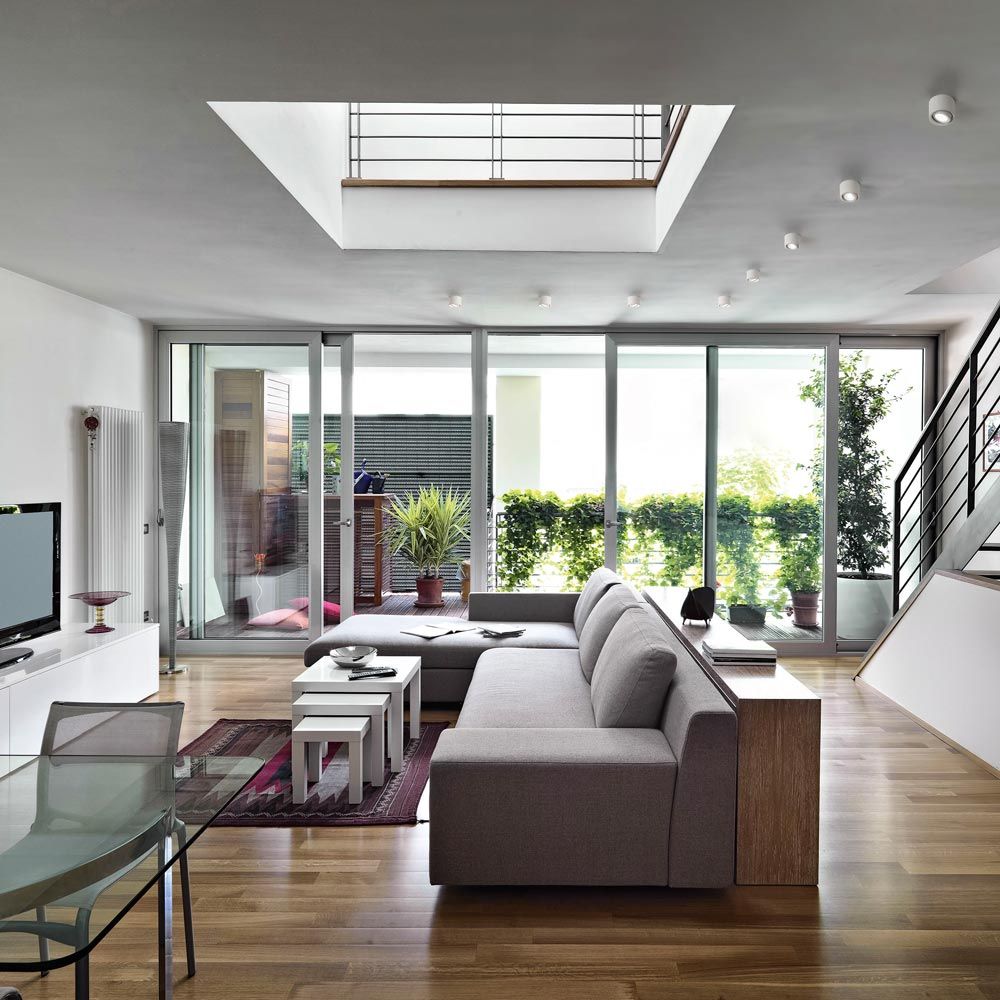 Helles Wohnzimmer mit moderner Einrichtung, großen Fenstern und Pflanzen für eine einladende Atmosphäre.