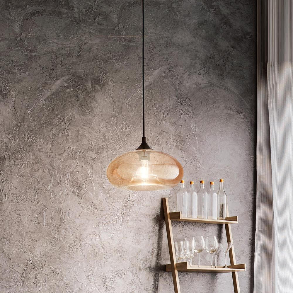 Ela Glas-Hängeleuchte in Amber über einem Holztisch mit Glasflaschen und Gläsern im Hintergrund.
