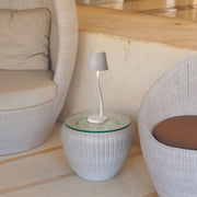 Judy LED Akku-Tischlampe mit Touch-Dimmer IP54 auf einem Tisch neben modernen Sesseln.