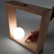 Kark LED Glas-Tischleuchte Holz mit einem massiven Eichenholzrahmen und einer Opalglaskugel.