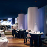 Elegante LED Pendelleuchte Delta Metall in modernem Restaurant-Ambiente mit stilvollen Tischen und Stühlen.