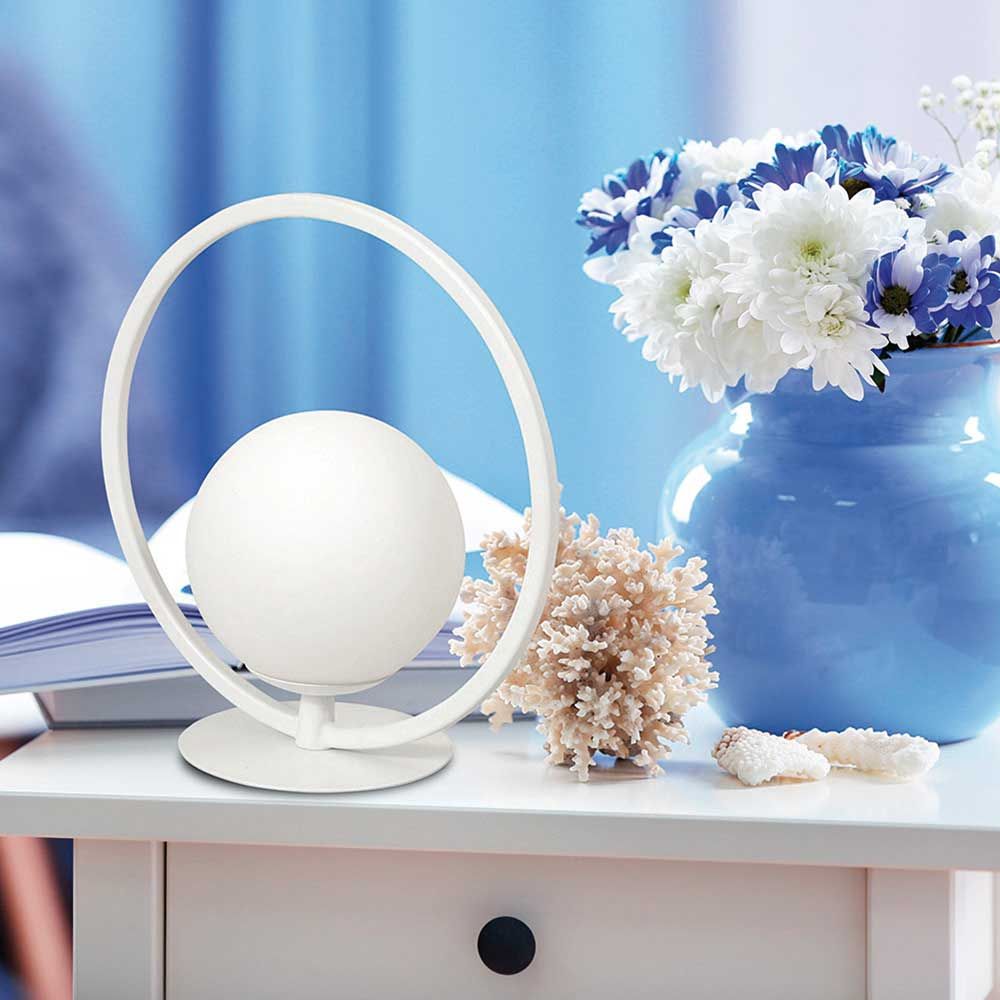 LED Tischlampe Sirio Rund auf einem Tisch mit Blütenvase und Buch im Hintergrund.