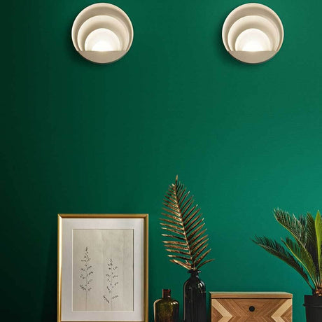 LED Wandleuchte Sunrise Ø26cm an grüner Wand mit Dekoration und Pflanzen.