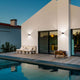 Lao LED Wandlampe IP65 Schwarz an einem modernen Haus mit Pool und Holzterrasse bei Abenddämmerung.