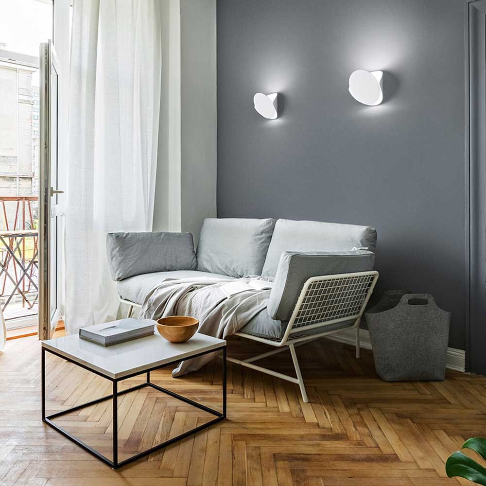 Moderner Raum mit Shield LED Wandleuchte aus Metall, grauer Couch und Holzboden.