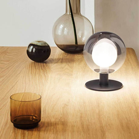 Teramo Tischbeleuchtung Ø 12cm auf einem Tisch mit dekorativen Vasen und einem Glas.