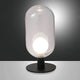 Tischleuchte Gubbio Ø 10cm auf schwarzem Untergrund mit glasklarer Kuppel und heller LED-Birne.