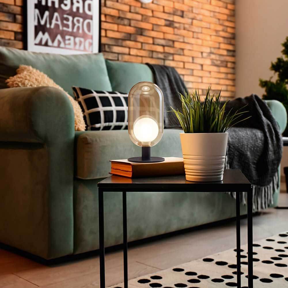 Tischleuchte Gubbio Ø 10cm auf einem Tisch neben einer Pflanze in einem modernen Wohnzimmer.