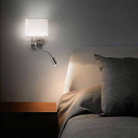 Moderne LED Wandleuchte Vietri neben einem Bett mit Kissen auf einem Nachttisch.