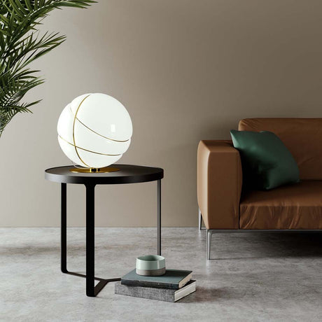 Fabbian Armilla table lamp, burnished, on a table next to a sofa with a plant in the background.