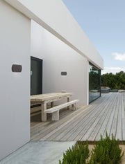 Fedor LED outdoor wall light 3000K anthracite IP65 on a modern wall beside a wooden table outdoors.