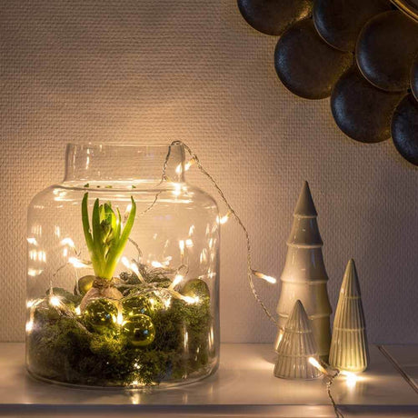 Feierliche LED Lichterkette IP20 dekoriert ein Glasgefäß mit Pflanzen und Lichtern in einem stilvollen Raum.