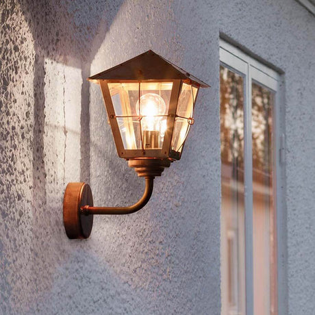 Fenix vegglampe for utendørs bruk i akrylglass, kobber, montert på en vegg, avgir varmt lys.
