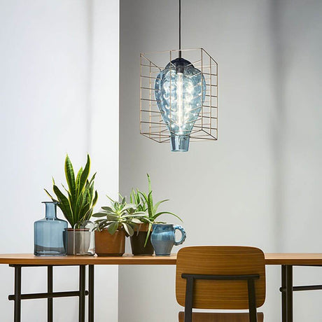 La lampe suspendue Attimo en verre de Murano dans une cage est suspendue au-dessus d’une table avec des plantes et des verres décoratifs.