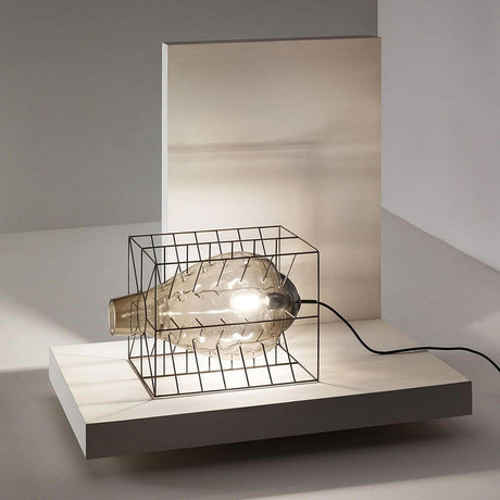 Attimo Tischlampe Muranoglas im Käfig auf einem minimalistischen Tisch mit Lichtscheinen.