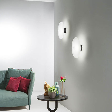 Desideria Wand- & Deckenlampe Satin, Schwarz an einer Wand über einem stilvollen Sofa.