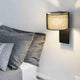 Fold Wandleuchte neben einem Bett mit grauen Kissen, modernes Design mit Stoffschirm und integriertem Schalter.