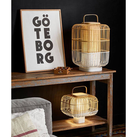 Forestier Bamboo Square Tischlampe auf einem Tisch, kombiniert mit einem Kunstwerk im Hintergrund.