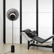 Forestier Stehlampe Oyster 145cm neben einem modernen schwarzen Lounge-Stuhl in einem minimalistischen Raum.