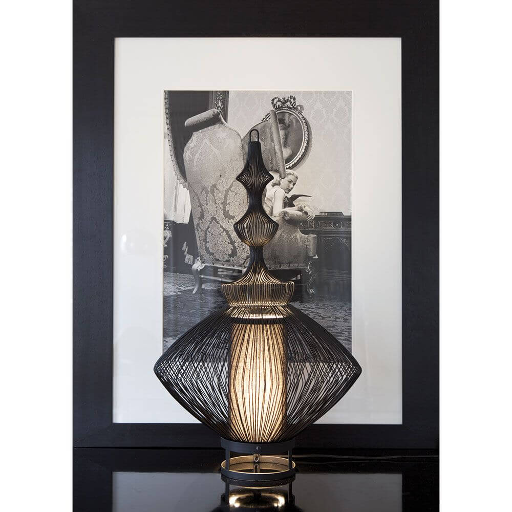 Forestier Tischlampe Opium mit metallischen Drähten und elegantem Design, im Vordergrund vor einem nostalgischen Bild.
