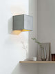 Gantlights B3 Wandlampe quadratisch Beton an Wand, grauer Betonwürfel mit goldener Innenbeschichtung und warmem Auf-/Abwärtslicht