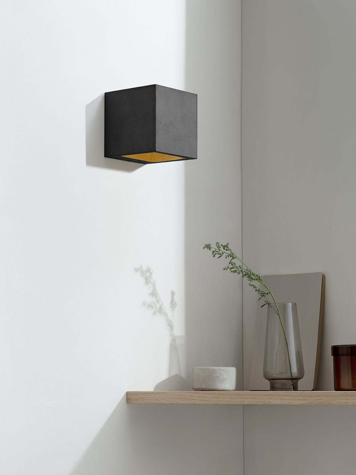 Gantlights B9 Wandleuchte Up & Down in schwarzem Beton mit goldener Innenseite an einer weißen Wand.
