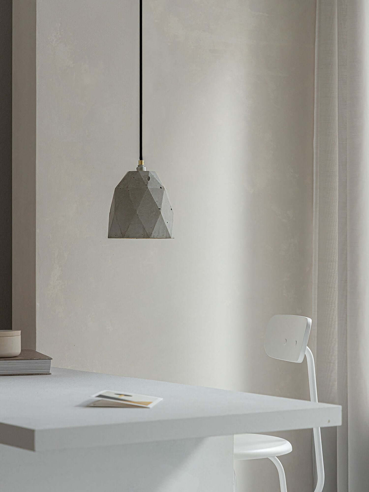 Gantlights T1 Pendelleuchte Beton hängt über einem modernen Tisch in einem minimalistischen Raum.