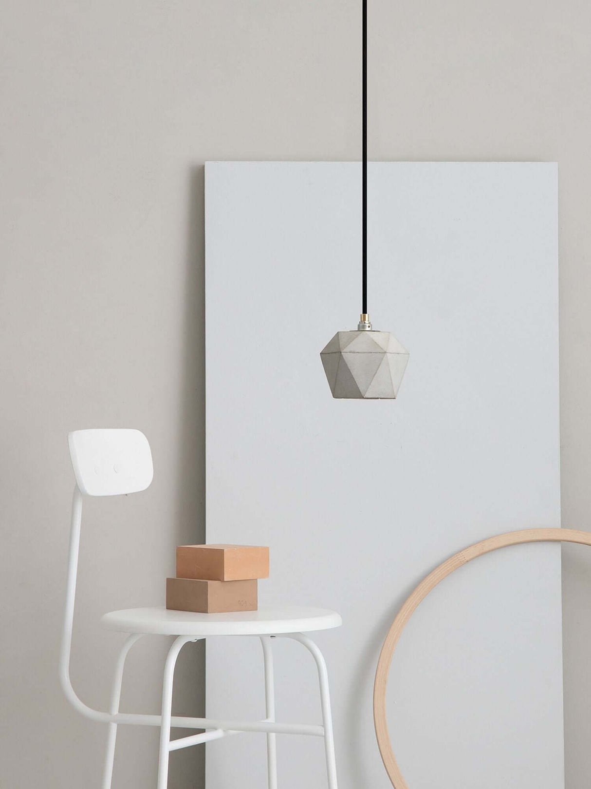 Gantlights T2 Hängelampe Beton dimmbar über einem weißen Stuhl mit Holzboxen und runder Holzform.