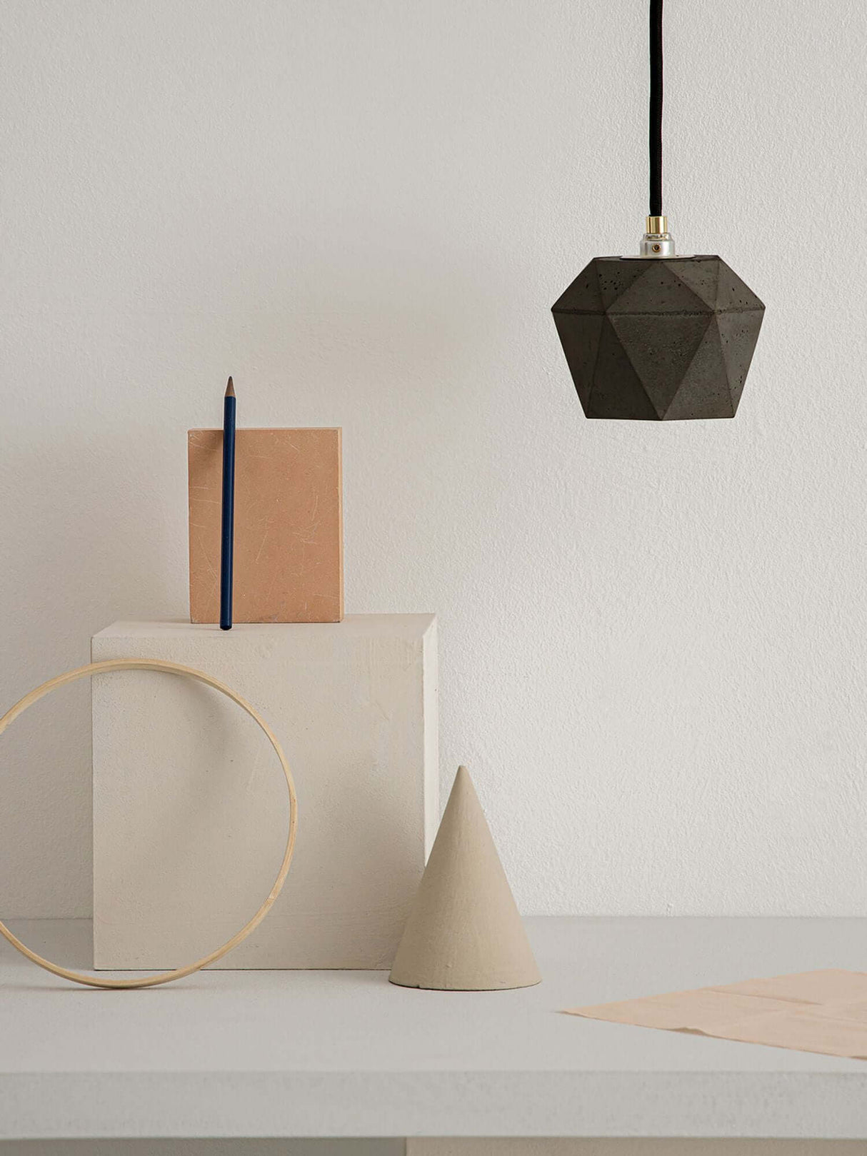 Gantlights T2 Hängelampe Beton dimmbar hängt über geometrischen Formen auf einem Tisch.
