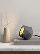 Gantlights T2-Up Tischlampe Beton auf einem Tisch mit geometrischem Design und goldener Innenseite.