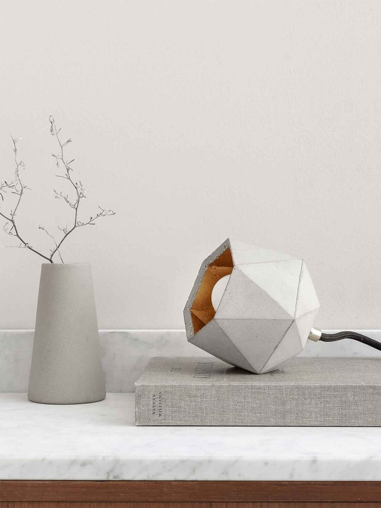 Gantlights T2-Up Tischlampe Beton auf Tisch mit grauem Vasen und Buch