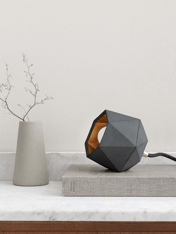 Gantlights T2-Up Tischlampe Beton auf einem Tisch mit geometrischem Design und goldener Innenseite.