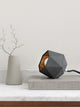 Gantlights T2-Up Tischlampe Beton auf einem Tisch mit geometrischem Design und goldener Innenseite.