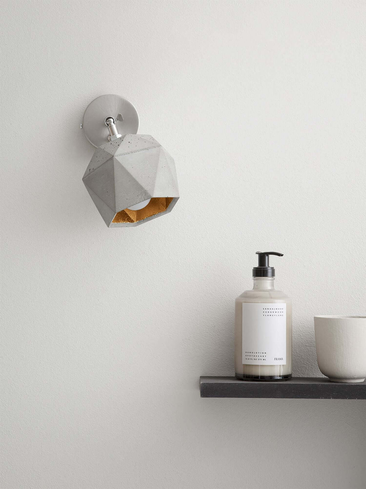 Gantlights T2 Wandspot Beton trianguliert an einer Wand, mit warmem Licht und dezenten Dekorationsobjekten.
