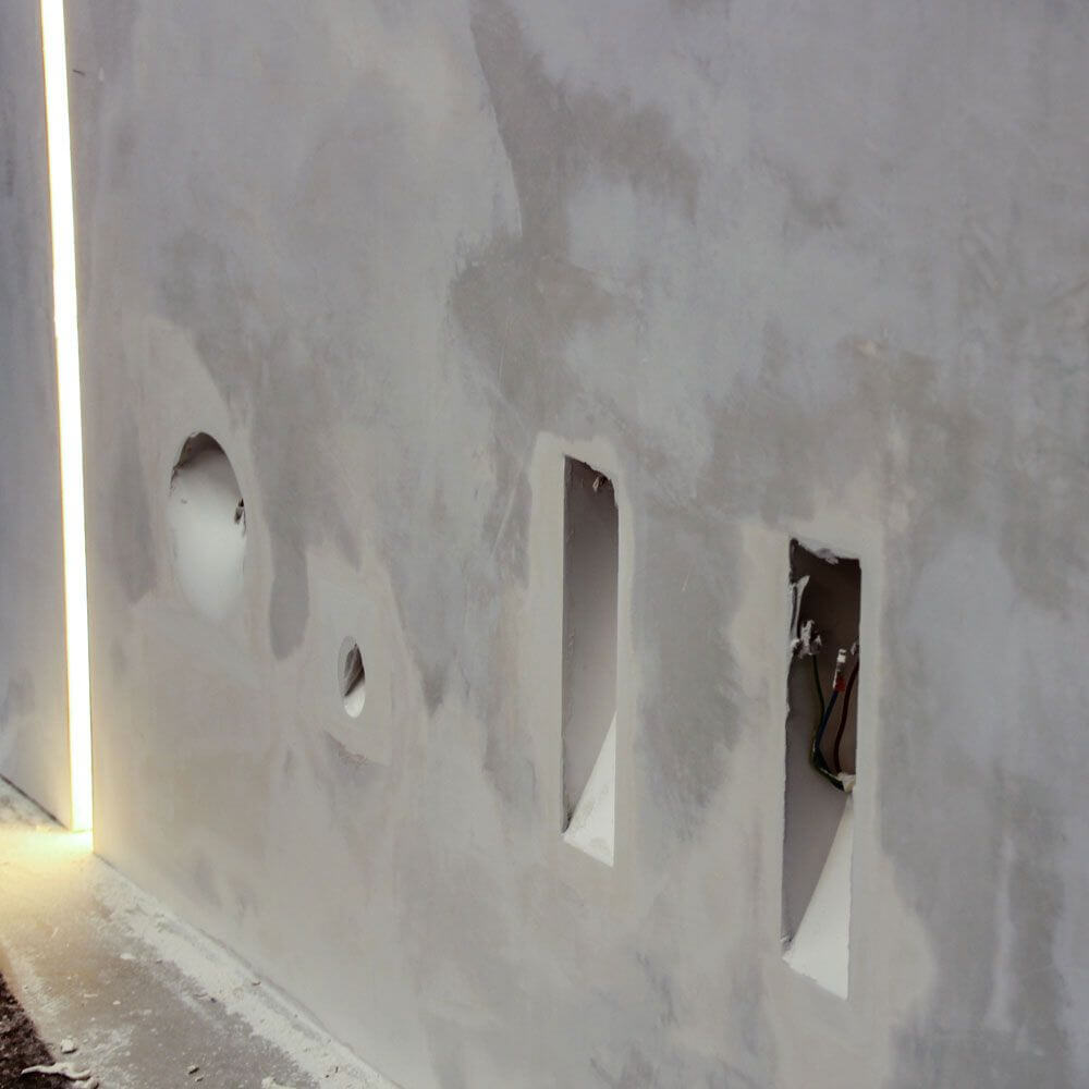 Einbauleuchten-Installationsöffnungen in einer Gipswand mit Lichtstreifen für akzentuierte Raumgestaltung.