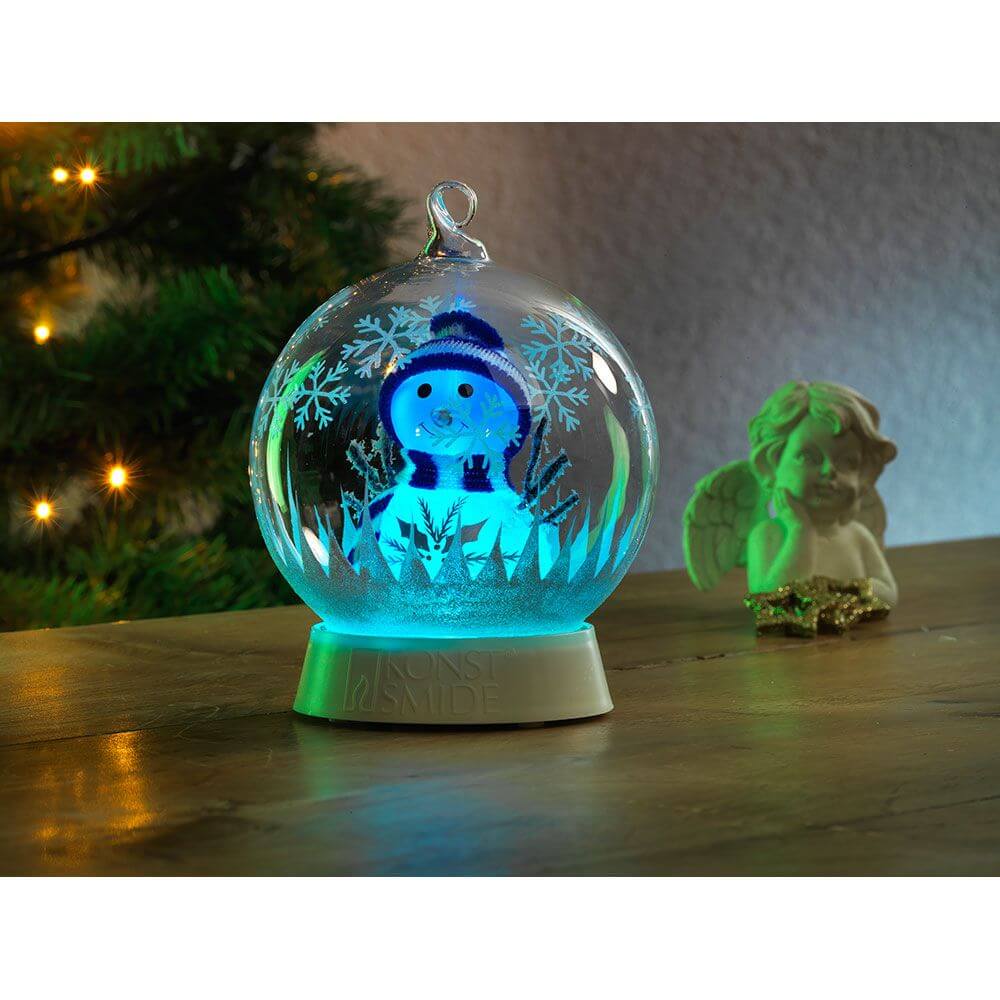 Glaskugel Schneemann mit 3 Funktionen Timer RGB-Farbwechsel 1 RGB Diode batteriebetrieben auf einem Holztisch.