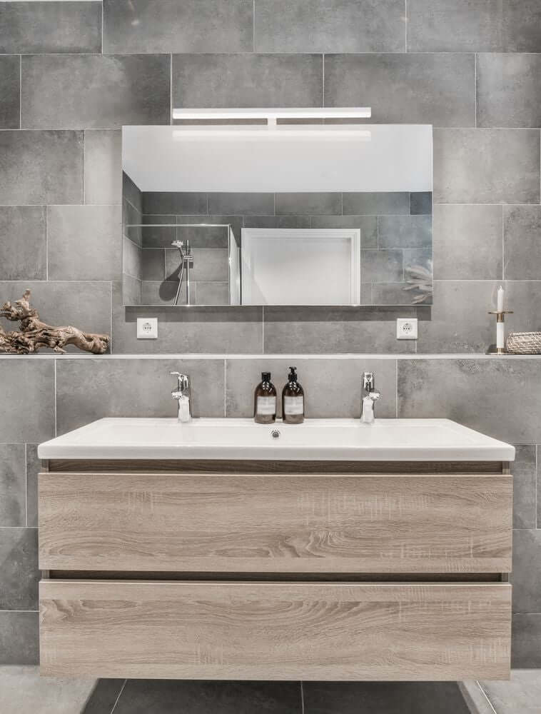 Glim LED Wandleuchte 3000K IP44 über einem modernen Badezimmerwaschtisch mit Holzfront.