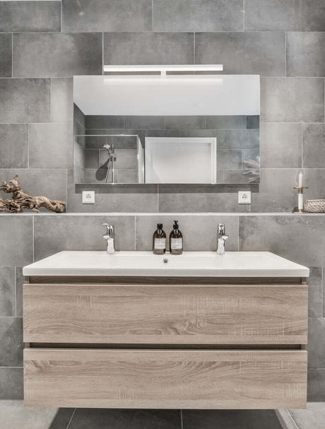Applique Glim LED 3000K IP44 au-dessus d’un lavabo de salle de bains moderne avec façade en bois.